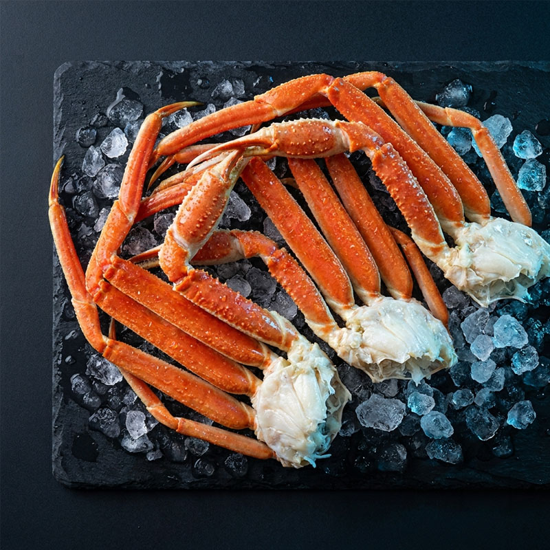 Three clusters of cooked snow crab legs on a bed of ice on a dark slate platter