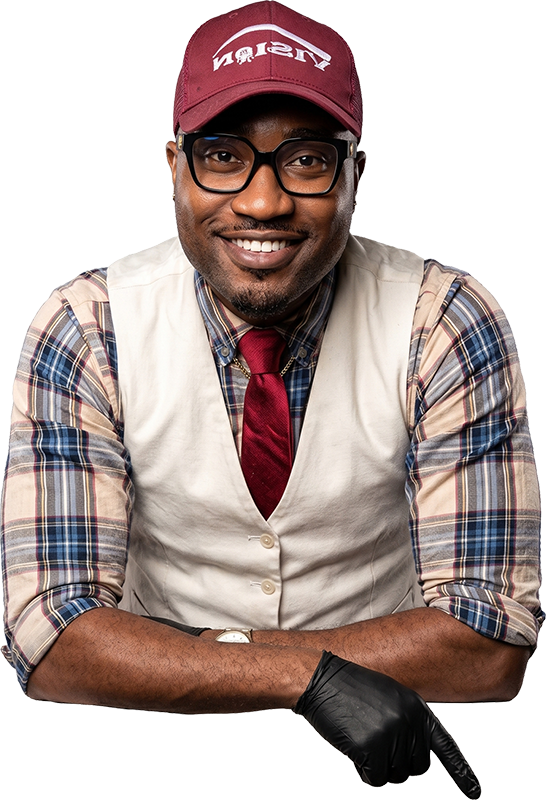 A smiling man in glasses and a cap, wearing a vest and tie, pointing down with a black gloved hand